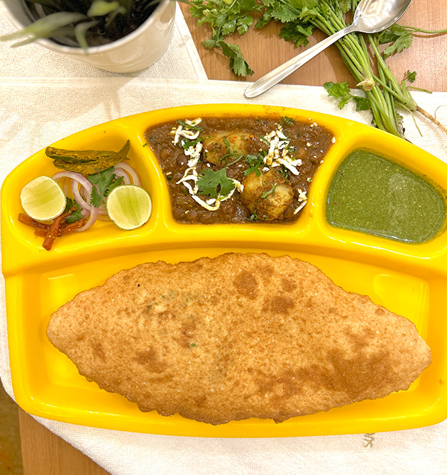 Chole bhature served on a yellow compartment tray with pickle, onion, lime and green chutney.