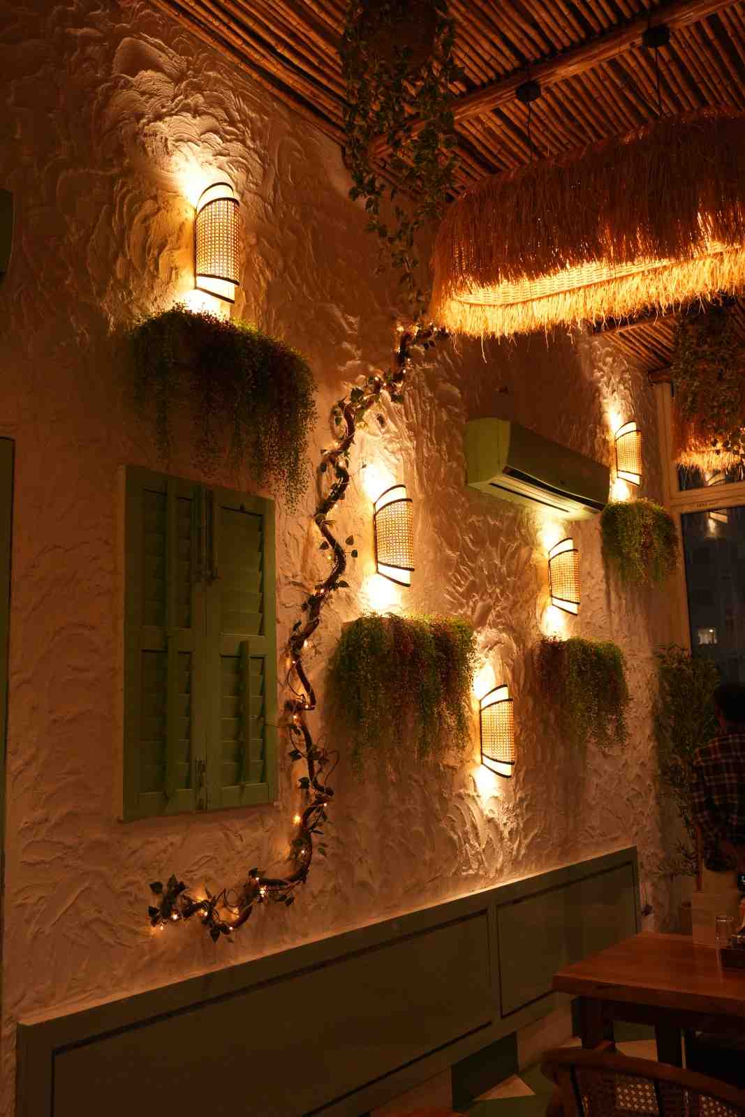 A wall of the cafe with warm sconce lighting, green shutters and trailing plants.