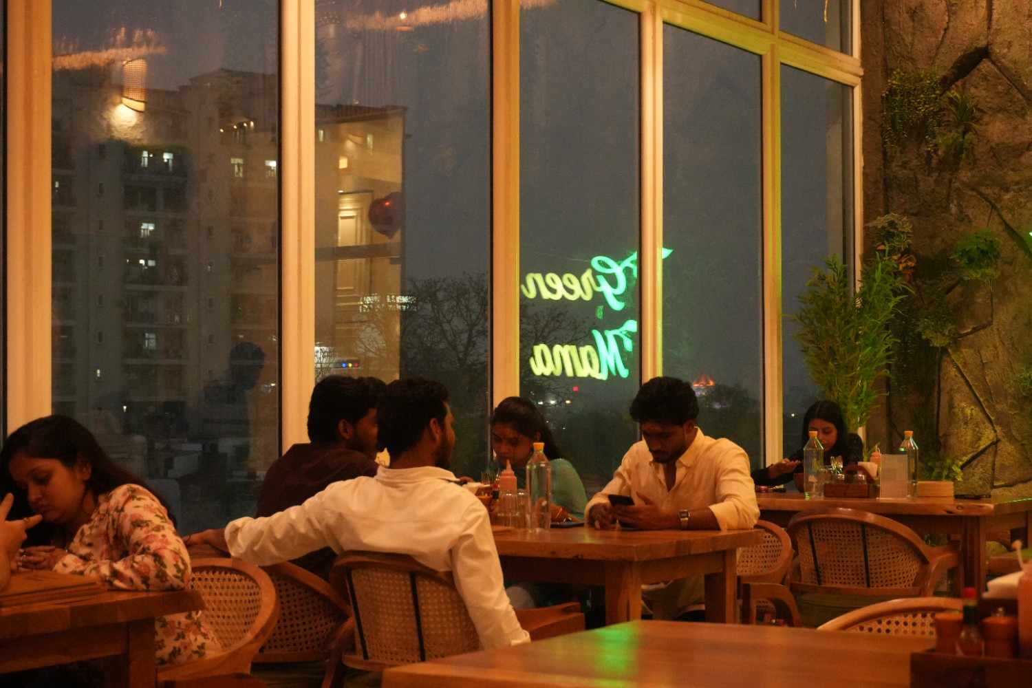 Guests at tables beside the windows in the evening, with the neon sign reflected in the glass.