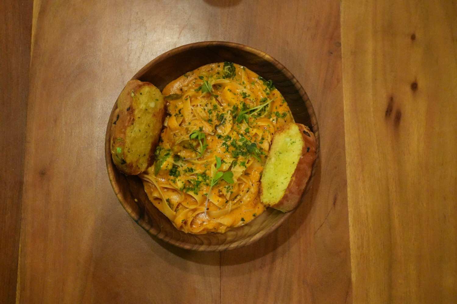 A bowl of creamy pasta topped with herbs and served with garlic bread.