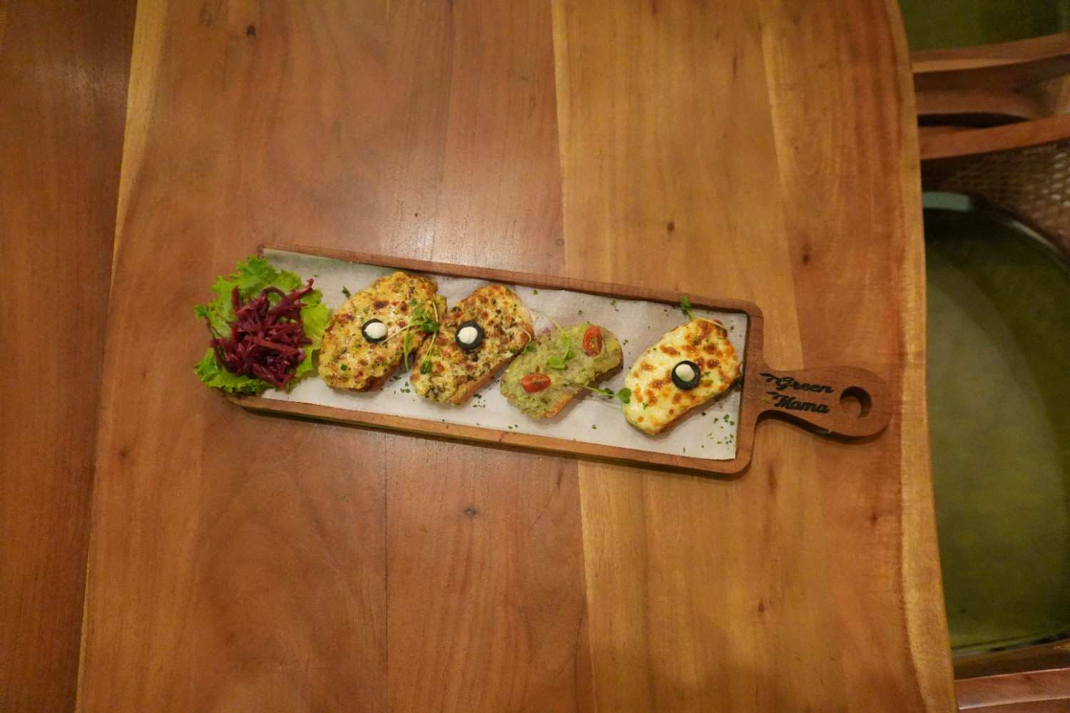 Four open toasts with toppings arranged on a long wooden serving board.
