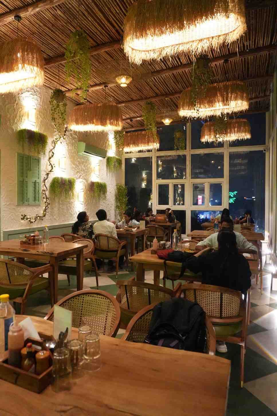 The dining room in the evening under cane pendant lamps, with guests at the tables.