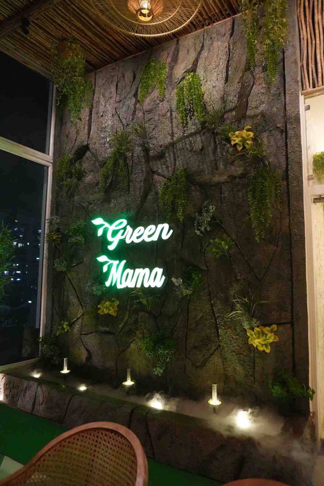 The green neon Green Mama sign glowing on a planted stone wall at night.