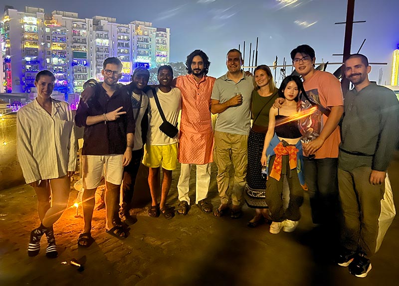 A large group of guests and hotel staff photographed together at night, with lit buildings behind them.