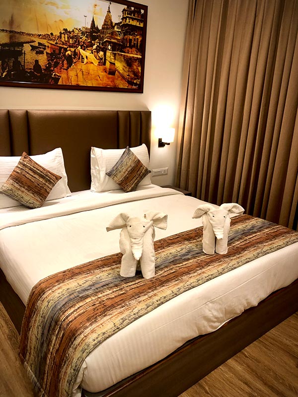A made bed with towels folded into shapes and a patterned runner.