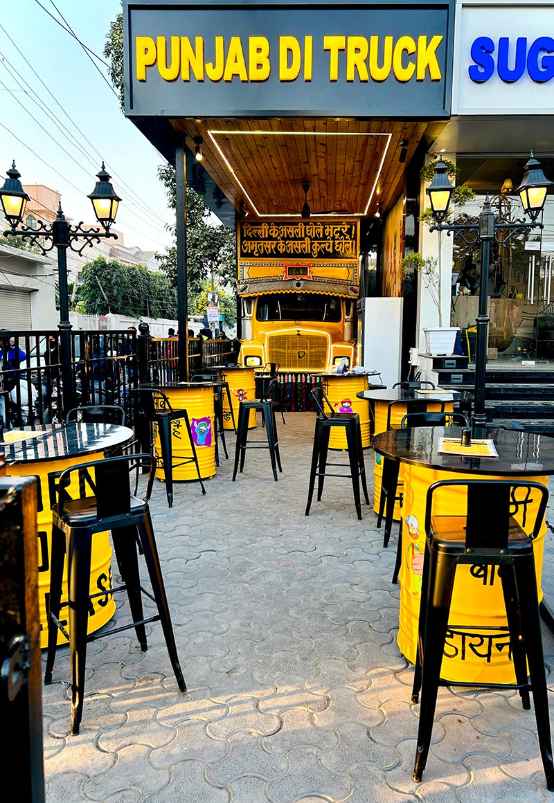 The Punjab Di Truck frontage with yellow bar stools and drum tables on the street.