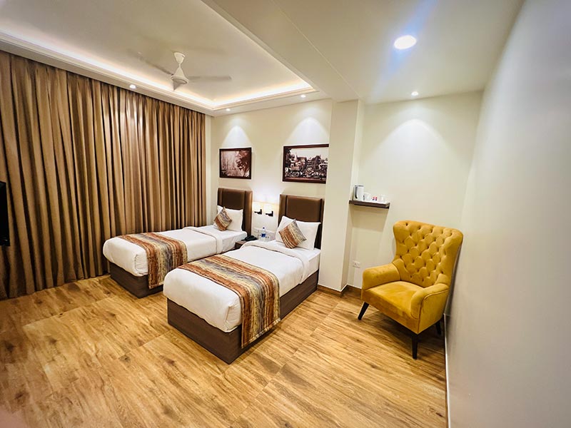 A room laid out with two single beds and a mustard armchair by the window.