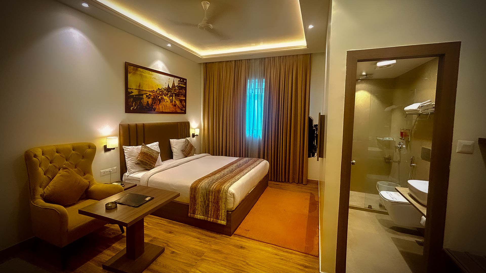 A deluxe room at night with cove lighting, a mustard armchair and the ensuite beyond.