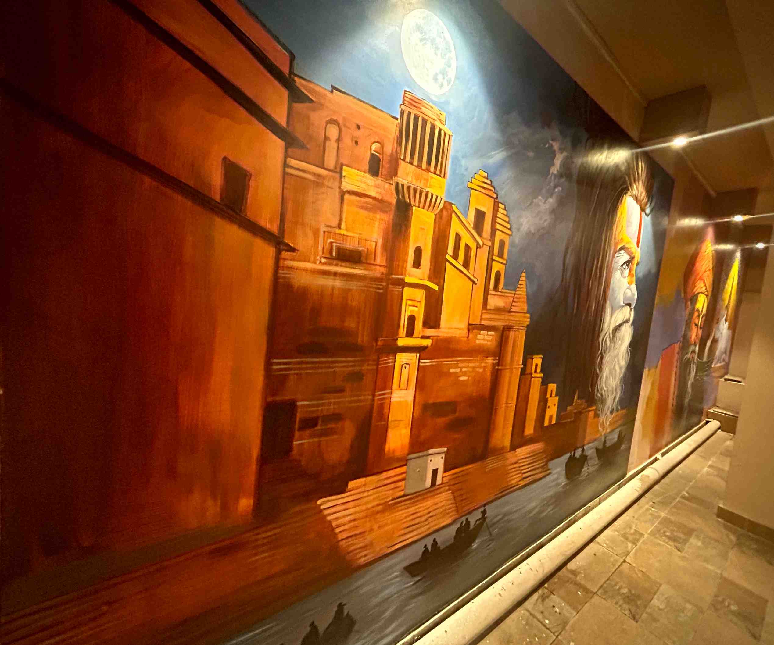 A long corridor mural of the moonlit ghats, with a sadhu's face painted into the night sky.