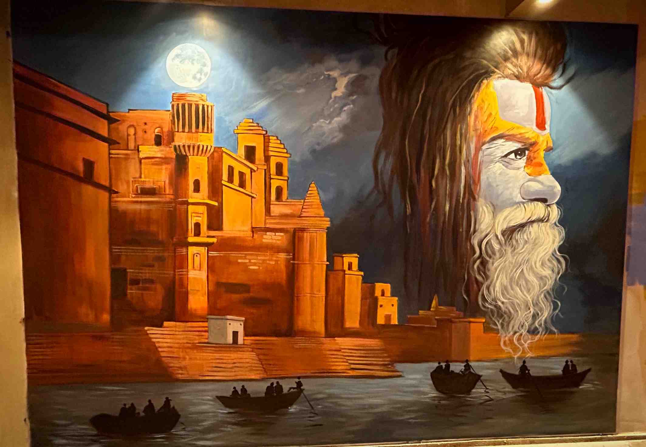A painted canvas of the moonlit Varanasi ghats with rowing boats and a sadhu's face in the sky.