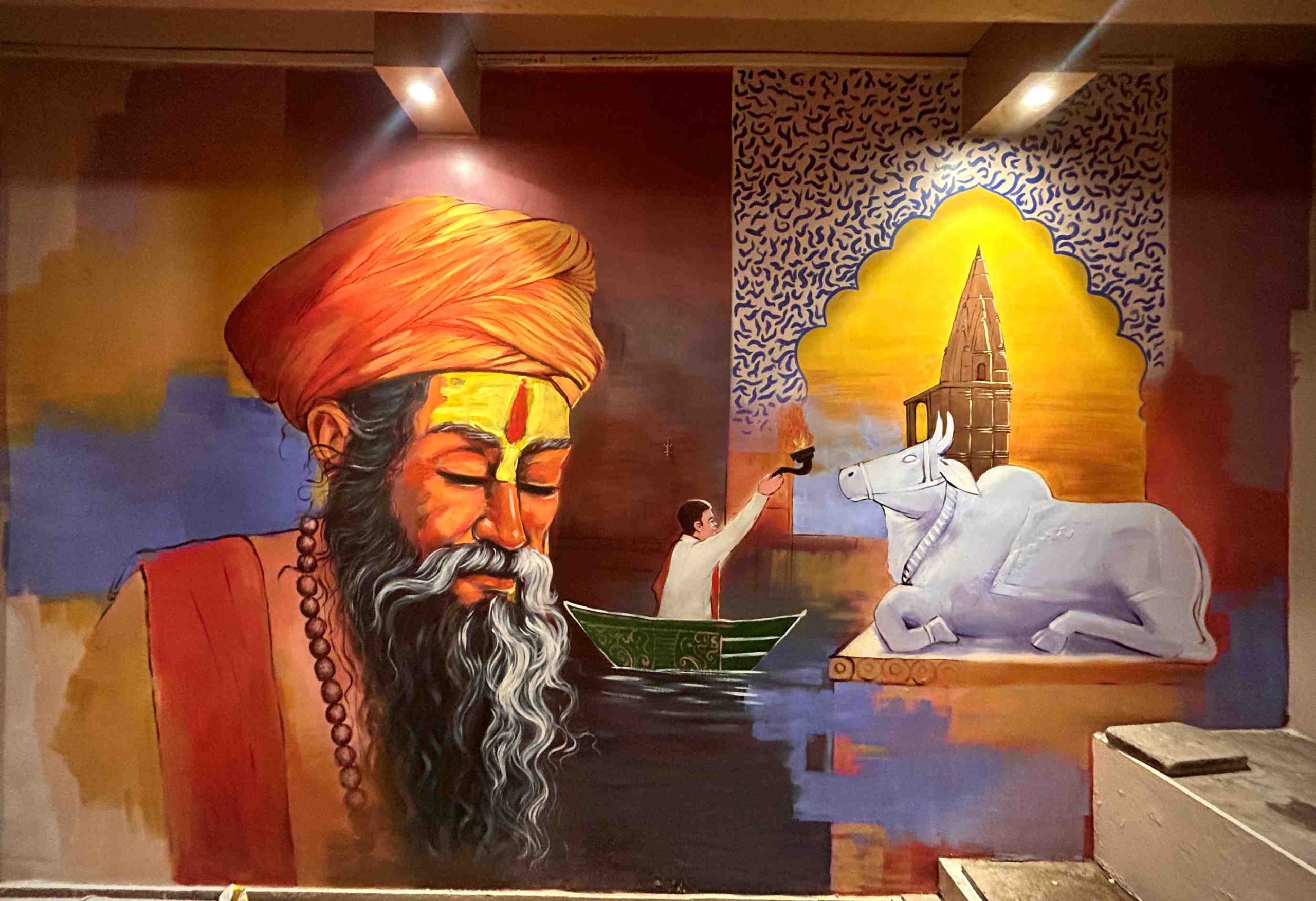 A mural of a saffron-turbaned sadhu beside a boatman raising an aarti lamp, with Nandi beneath an arch.