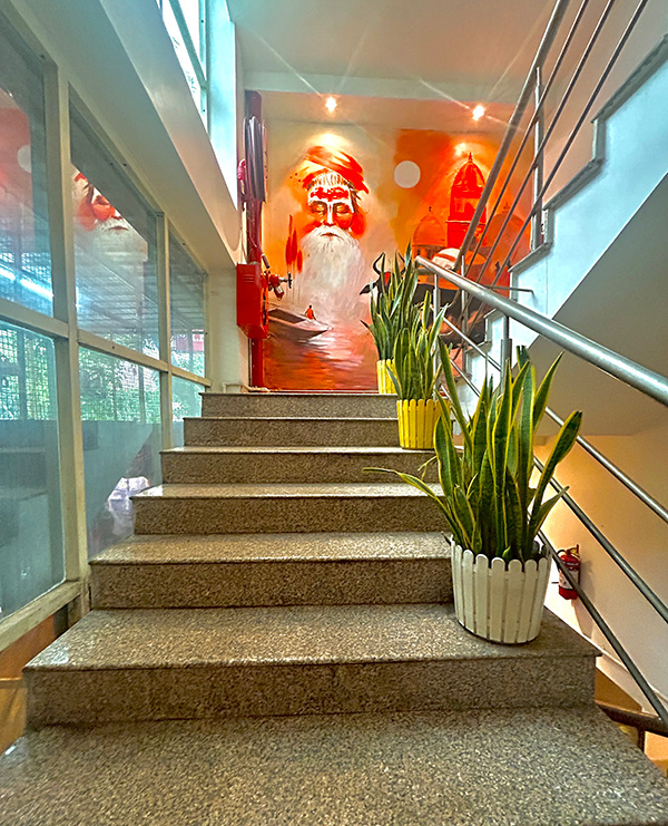 A staircase rising towards a painted mural of a sadhu, with snake plants on the steps.